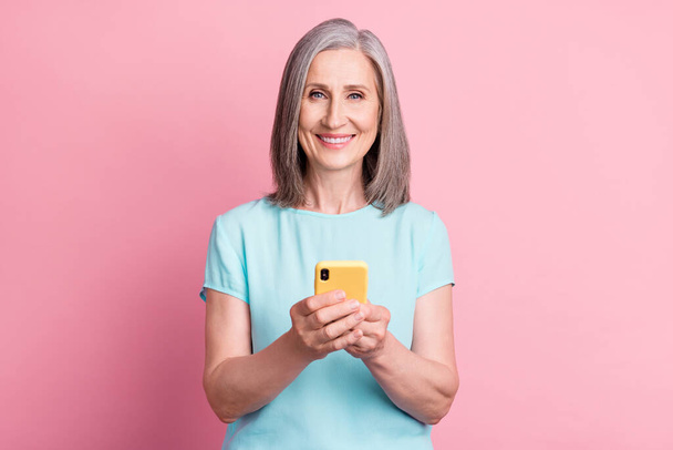 Photo of funky aged grey hairdo lady hold telephone wear teal blouse isolated on pink color background - Foto, afbeelding