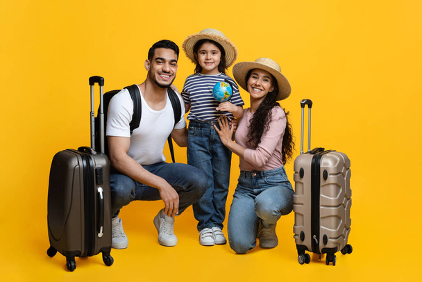 Rodinné cestování. Veselí arabští rodiče a malá dcera s kufry přes žluté pozadí - Fotografie, Obrázek