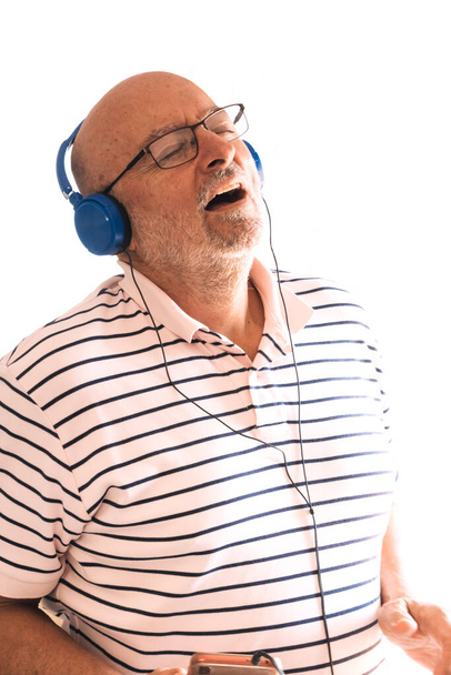 Homem velho feliz em fones de ouvido cantando com fundo de parede, isolado com copyspace.  - Foto, Imagem