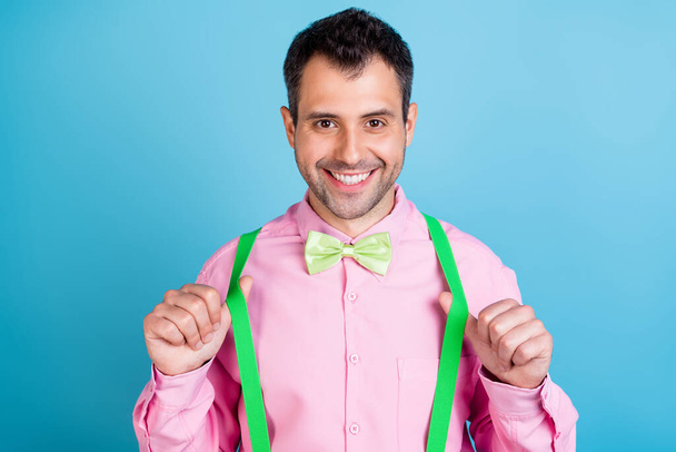 Photo of trend brunet hairdo young man hold suspenders wear pink shirt isolated on blue color background - Fotoğraf, Görsel