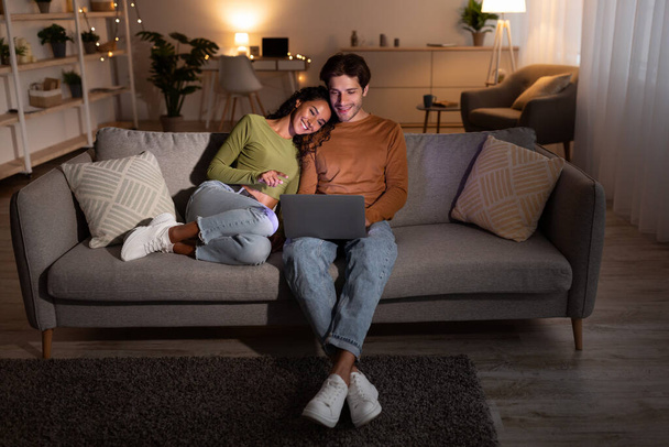 Casal assistindo filme no laptop sentado no sofá em casa
 - Foto, Imagem