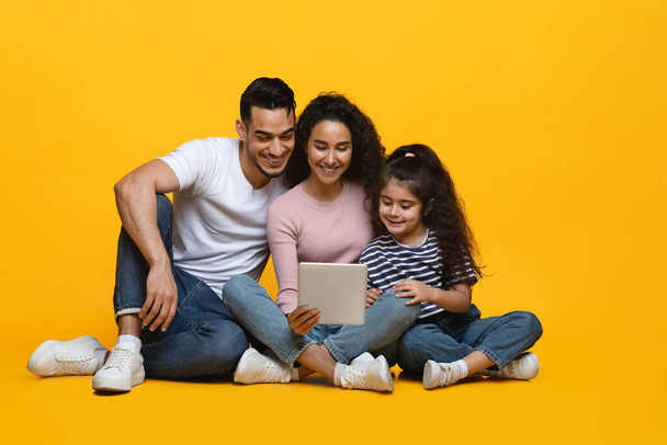 Ευτυχισμένη Μεσανατολίτικη οικογένεια των τριών με ψηφιακή ταμπλέτα σε κίτρινο φόντο στούντιο - Φωτογραφία, εικόνα