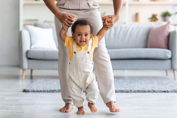 Adorable black infant boy making first steps at home with mothers help - Zdjęcie, obraz