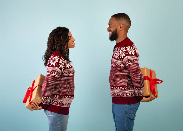 Liebevolle afrikanisch-amerikanische Männer und Frauen halten Weihnachtsgeschenke hinter ihrem Rücken, tauschen Geschenke, blauer Hintergrund - Foto, Bild