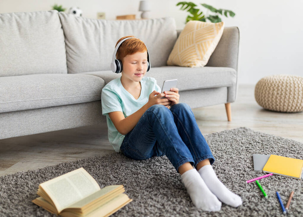 Criança pré-adolescente usando fone de ouvido e smartphone enquanto faz lição de casa - Foto, Imagem
