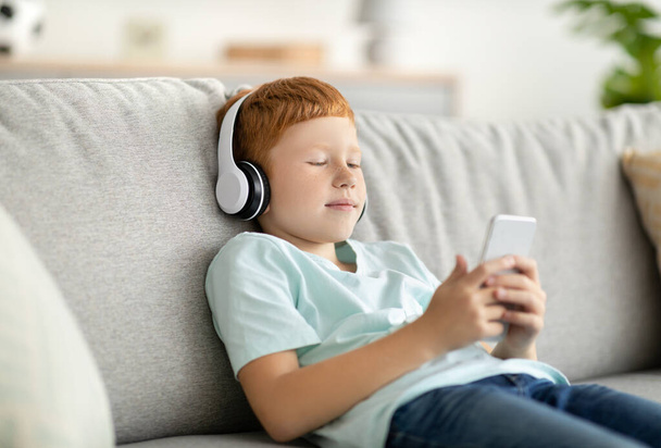 Preteen boy watching videos on mobile phone, using headset - Photo, Image