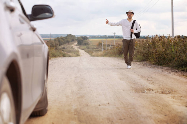 A man walks along a country road. Hitchhiker around the country. A man stops a passing car on road. - Fotoğraf, Görsel