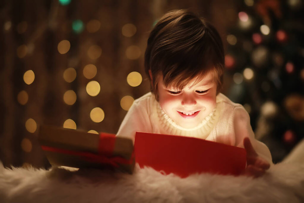 Семья накануне Рождества у камина. Дети открывают рождественские подарки. Дети под елкой с подарочными коробками. Оборудованная гостиная с традиционным камином. Уютный теплый зимний вечер. - Фото, изображение