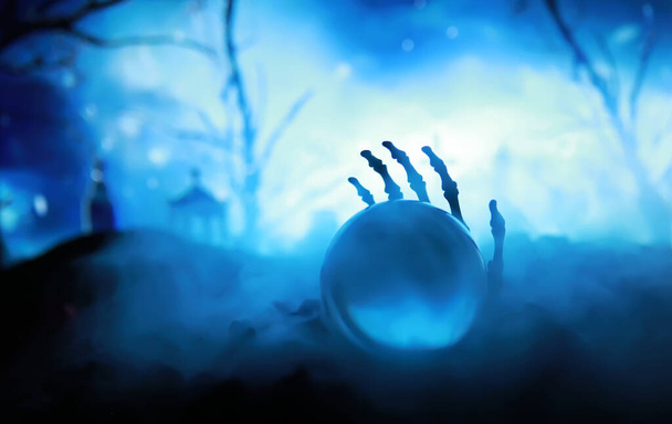 Esqueleto zombi mano levantándose de un cementerio - Halloween. Misteriosas predicciones de bolas mágicas y humo en la escena oscura. Cajero de fortuna, poder mental, concepto de predicción. fondo misterioso - Foto, imagen