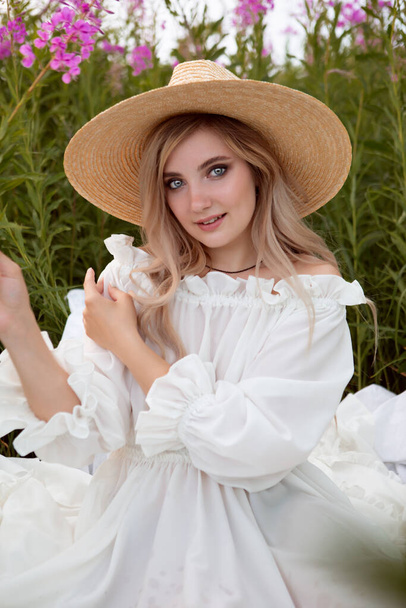 A gorgeous romantic young woman in a white light dress and a straw hat. Fashionable portrait of a sexy girl - Foto, imagen