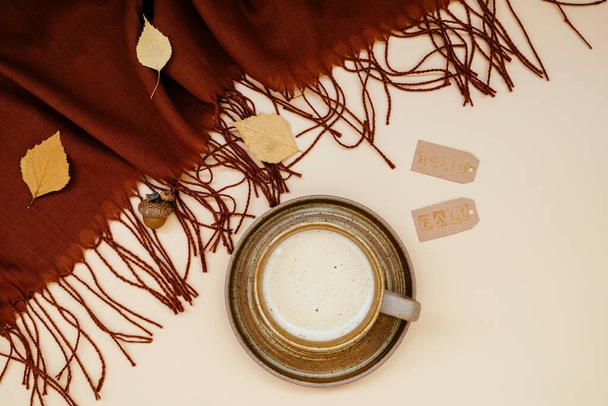Ατμοσφαιρική φθινοπωρινή σύνθεση. Πτώση φόντο με κούπα του καφέ, βαθύ καφέ κασκόλ κασμίρ και φύλλα σε παστέλ χρώματα. Κυριακάτικη χαλάρωση, αναμνήσεις και νεκρές φύσεις. Επίπεδη. Εστίαση στο φόντο - Φωτογραφία, εικόνα