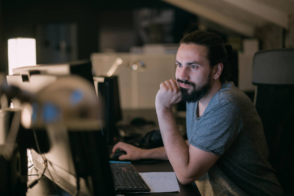Este egy fiatalember dolgozik az irodában a monitorok előtt. Jóképű fickó sok monitor előtt ül egy modern irodában késő este.. - Fotó, kép