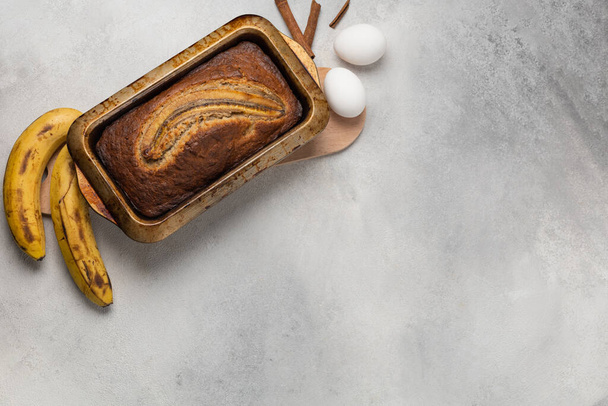 Ready fresh banana bread in a rectangular baking dish with ingredients on a light background - Foto, Bild
