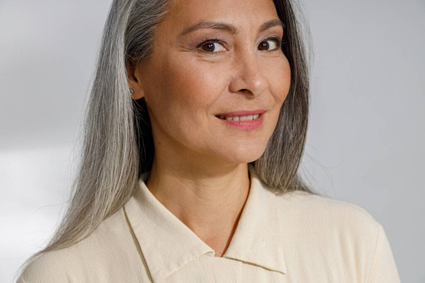 Belle dame mature aux cheveux gris en chemise élégante sourit à la caméra en studio - Photo, image