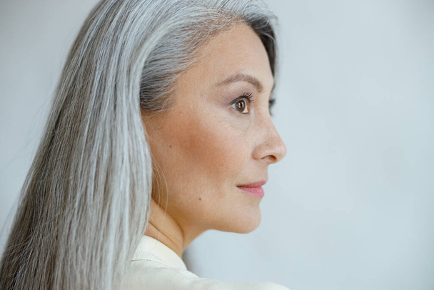 Középkorú ázsiai nő gyönyörű egyenes hoary haj világosszürke háttér - Fotó, kép