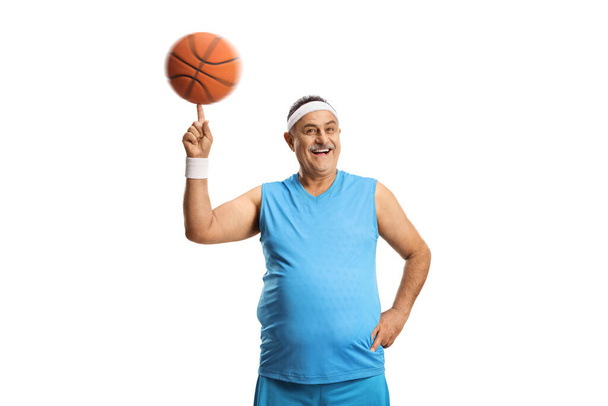 Cheerful mature man spinning a basketball with his finger isolated on white background - Zdjęcie, obraz