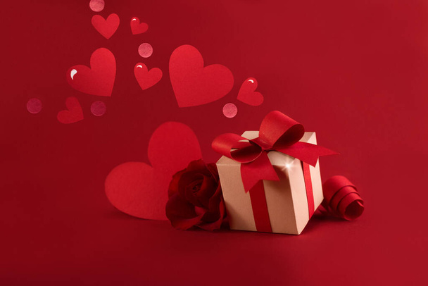 Happy st. Valentines day concept with craft paper gift box, red paper hearts, bows against dark red background with empty space for text. - Photo, Image