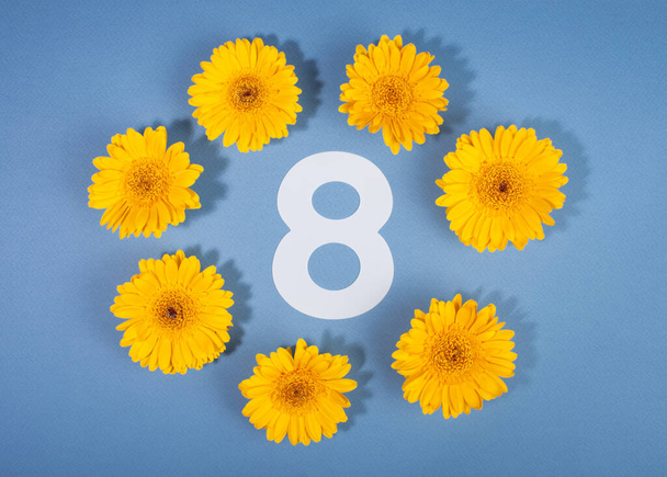 Number 8 surrounded with yellow gerbera flowers on blue background. - Valokuva, kuva