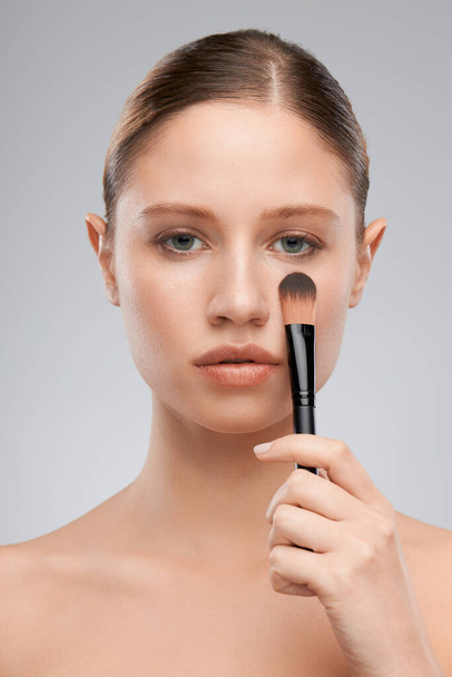 Gorgeous young lady holding makeup brush and posing in studio. Beauty photography - Photo, Image