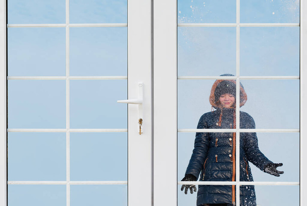 Winter view from a plastic window. Young girl playing in the snow - 写真・画像