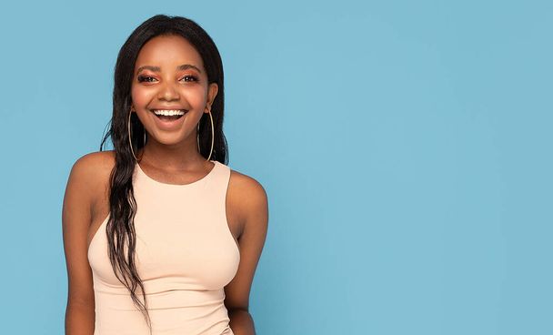 Real people emotions. Beautiful smiling african american woman with glamour makeup and long dark hair looking at the camera. Happiness. Blue pastel background. - Foto, immagini