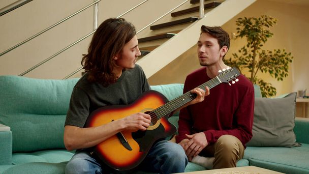 Ένας νεαρός παίζει κιθάρα για τον φίλο του και τραγουδούν και οι δύο. - Φωτογραφία, εικόνα