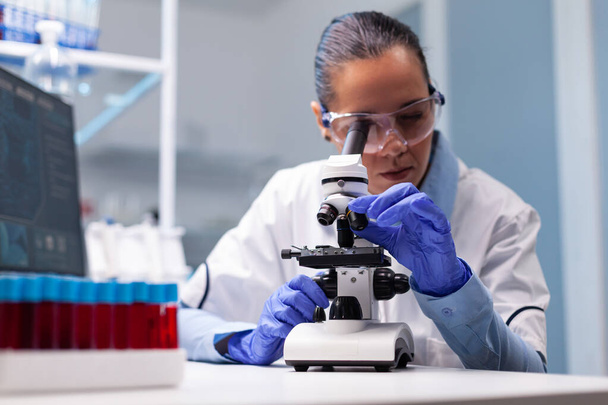 Microbiologiste médecin femme analyse les résultats du vaccin à l'aide d'un microscope médical - Photo, image