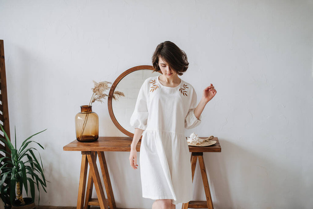 Looking down young woman in summer dress inside a room. Pretty brunette with short hair indoors. Mirror in background. Longshot. - Foto, imagen