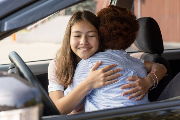 Sevimli, neşeli bir kız ve annesi arabada kucaklaşıyorlar. - Fotoğraf, Görsel