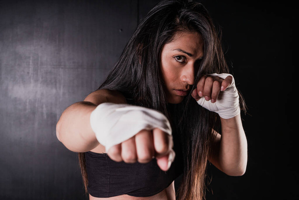 Молодая латиноамериканка занимается боксом и кикбоксингом. Она наносит прямой удар кулаком. Дифференциальный фокус. Спорт, фитнес, фитнес, концепция тренировок. - Фото, изображение