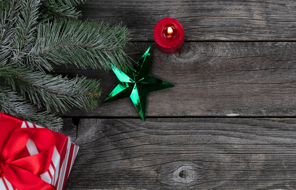 Pojedyncza zielona ozdoba gwiazdy i świecące świece, pudełko prezentów plus dekoracje gałązki śniegu na rustykalnych drewnianych deskach do Wesołych Świąt Bożego Narodzenia lub szczęśliwego Nowego Roku święto koncepcja   - Zdjęcie, obraz