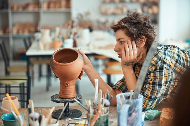 Charming female potter painting pottery in workshop - 写真・画像