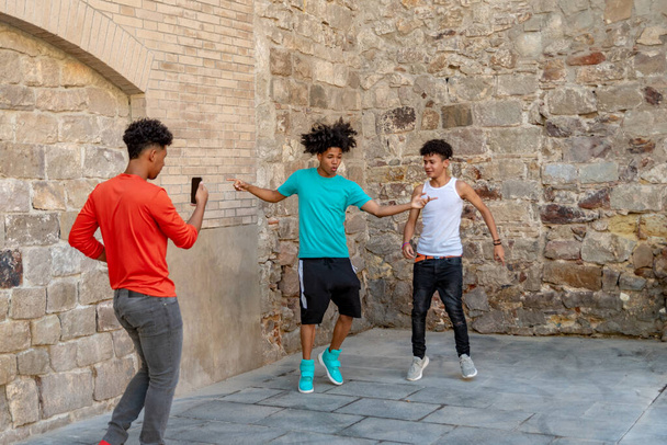 アフリカのラテン系の男性の10代の友人が路上で踊り、携帯電話でそれを記録します。スペースのコピー - 写真・画像
