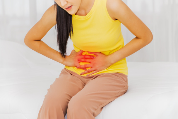 腹部の痛みと健康管理の概念を持つ女性:アジアの女性は、腹部の痛みとベッドに座っています,異常な腹部の臓器,おそらく月経.. - 写真・画像
