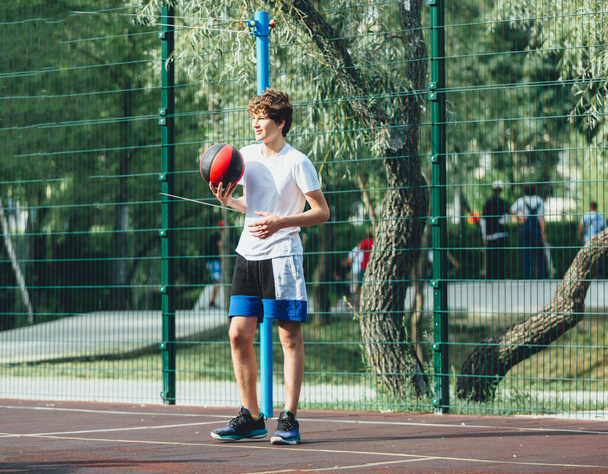 Sevimli genç, şehir parkında basketbol oynuyor. Bir çocuk dışarıda elinde bir basketbol topu tutuyor. Aktif hayat, hobi, çocuklar için spor - Fotoğraf, Görsel