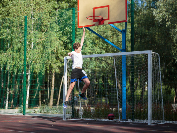 Cute teenager plays basketball at a city playground. A boy holds a basketball ball in his hands outside. Active life, hobby, sports for children - Fotoğraf, Görsel