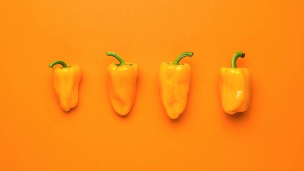 Чотири стиглі апельсинові перець на оранжевому фоні. Вегетаріанська їжа. Свіжий урожай овочів.. - Фото, зображення