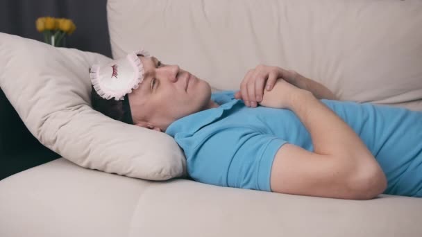 Schläfriger Mann liegt auf dem Sofa, zieht Augenbinde über die Augen - Filmmaterial, Video
