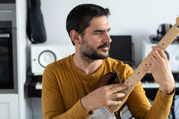 young boy with beard playing guitar at home with piano on the back - Foto, Bild