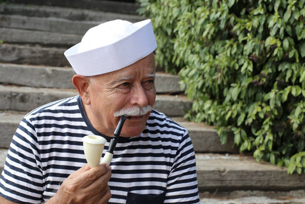 Nahaufnahme Porträt eines gut aussehenden älteren Mannes im Matrosenkostüm, der draußen Pfeife raucht - Foto, Bild