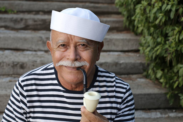 Nahaufnahme Porträt eines gut aussehenden älteren Mannes im Matrosenkostüm, der draußen Pfeife raucht - Foto, Bild