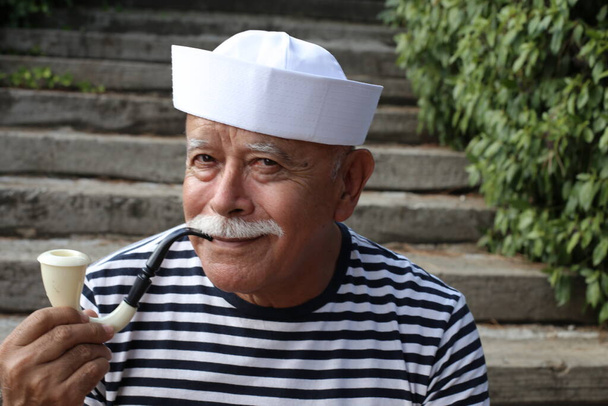zbliżenie portret przystojny senior mężczyzna w marynarz kostium palenie fajki na zewnątrz - Zdjęcie, obraz