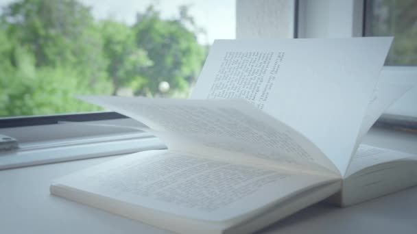 Un libro yace en el alféizar de una ventana abierta, los rayos del sol en las páginas, primer plano - Imágenes, Vídeo