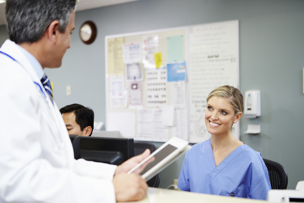 Doctor In Discussion With Nurse At Nurses Station - 写真・画像