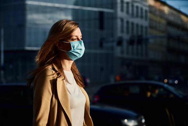 Beautiful caucasian woman wearing protective medical mask at city street. Portrait of millenial woman. Social distance and protect from coronavirus - Φωτογραφία, εικόνα