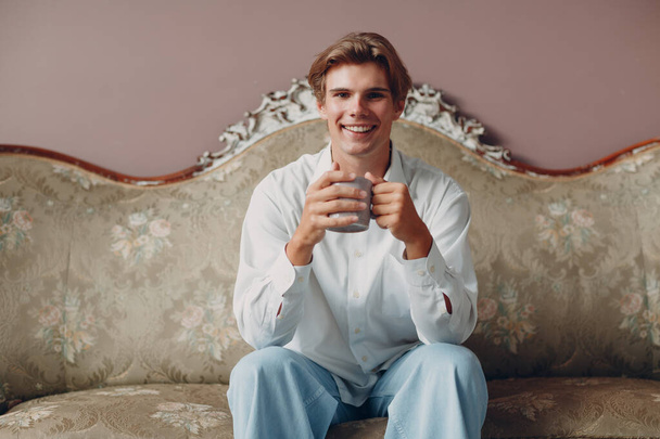 Портрет молодого человека, сидящего и пьющего и наслаждающегося послеобеденным чаем или кофе - Фото, изображение