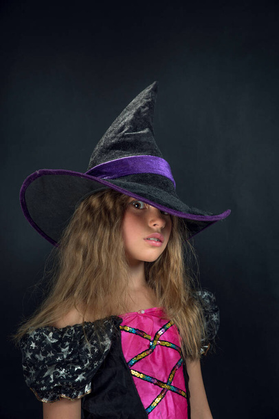 Ένα κορίτσι ντυμένο σαν μάγισσα και ένα πλατύ καπέλο για το Χάλογουιν.. - Φωτογραφία, εικόνα