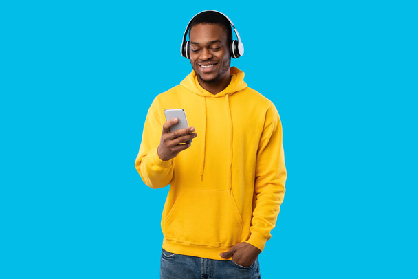 African Guy In Headphones Using Smartphone Listening Music, Blue Background - Zdjęcie, obraz