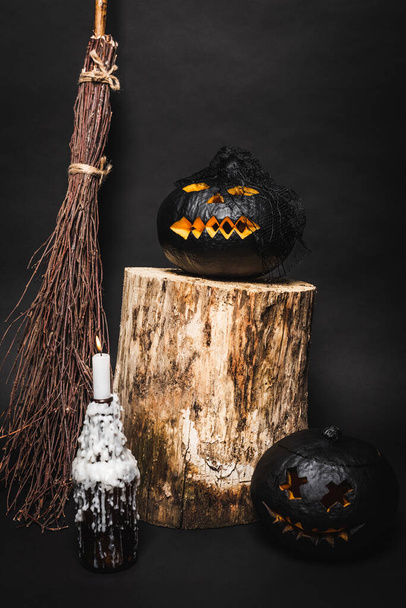 broom near dark pumpkin on wooden stump near burning candle on black  - Photo, Image