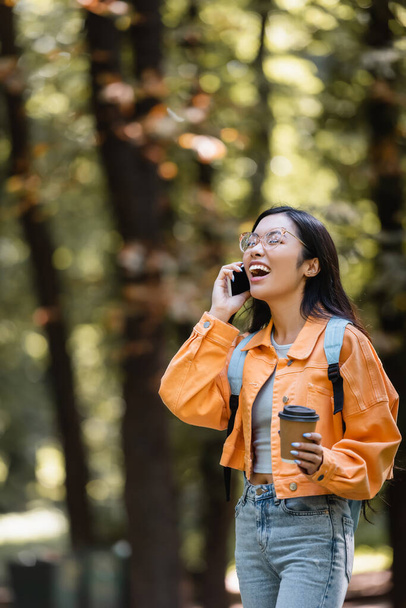asian student laughing with closed eyes while talking on smartphone outdoors - Foto, Imagem